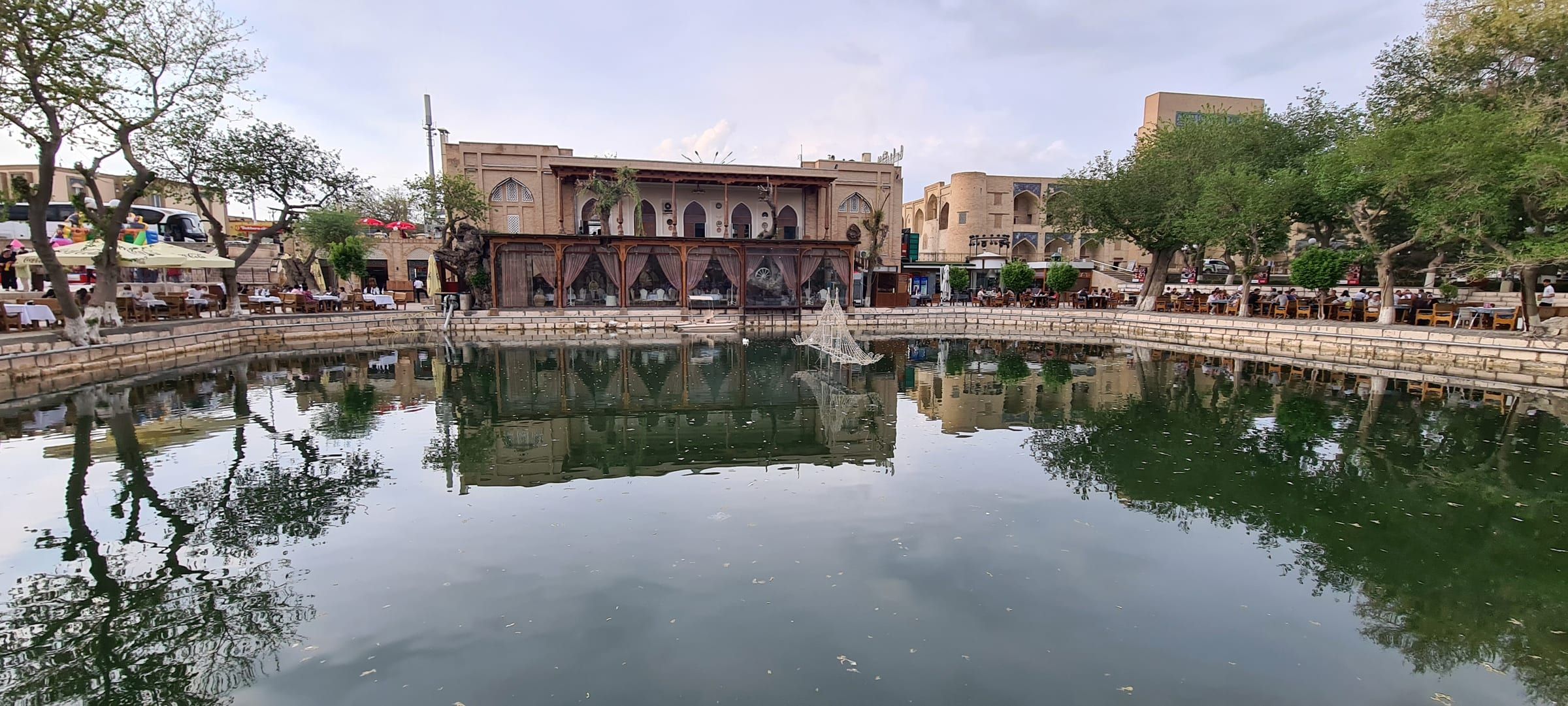 The pool at Lyabi-Hauz in Bukhara in the evening, old mulberry trees and madrasas around it.
