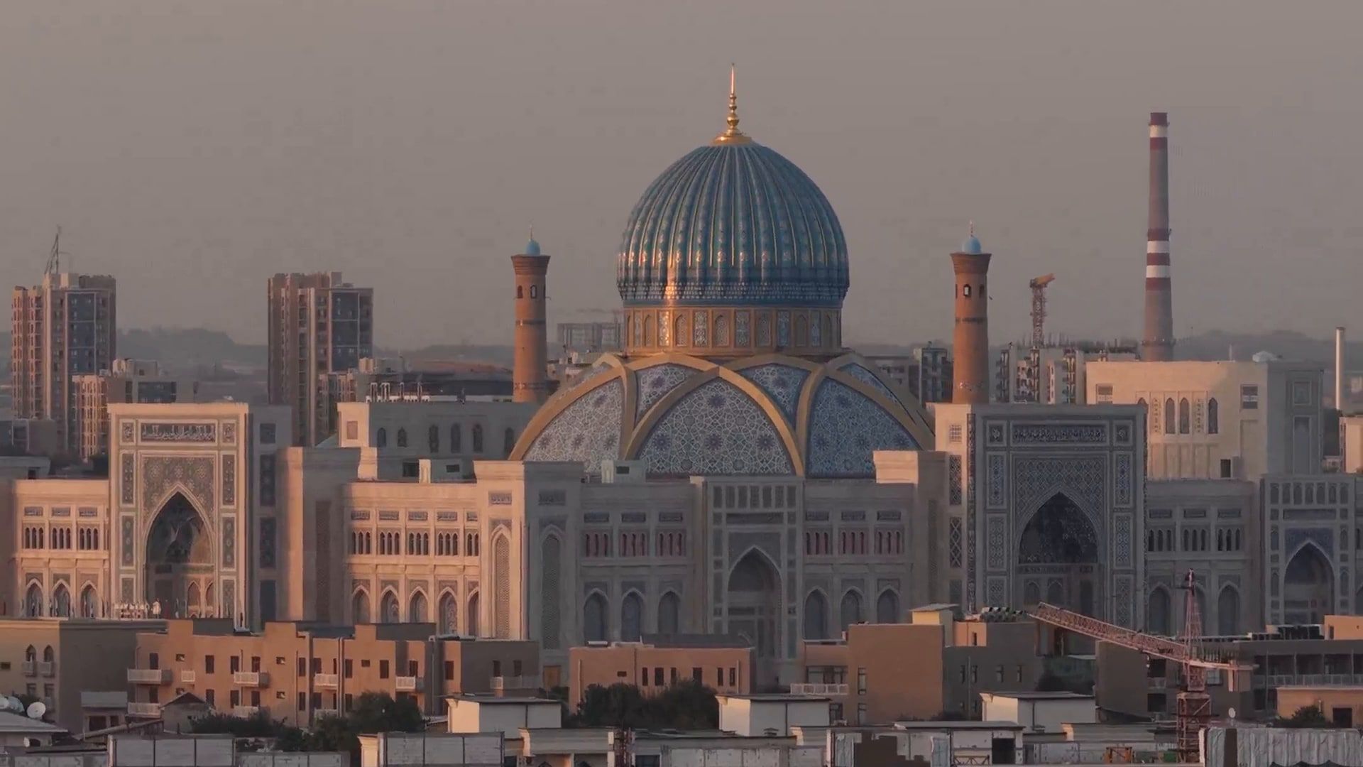 Tashkent from above at sunset, a great tiled dome and minarets rising over the rooftops of the city.